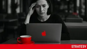 Mladá žena zamyšleně sedí v kavárně u notebooku s chatgpt, přemýšlí nad podnikatelským nápadem. Černobílá fotografie s červeným akcentem na šálku a logu na notebooku.