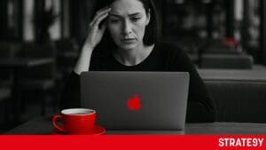 Mladá žena zamyšleně sedí v kavárně u notebooku s chatgpt, přemýšlí nad podnikatelským nápadem. Černobílá fotografie s červeným akcentem na šálku a logu na notebooku.